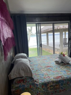 Ein Hotelzimmer mit Bett, Blick auf das Meer durch eine Glastür und einem Strohdachschirmchen draußen.