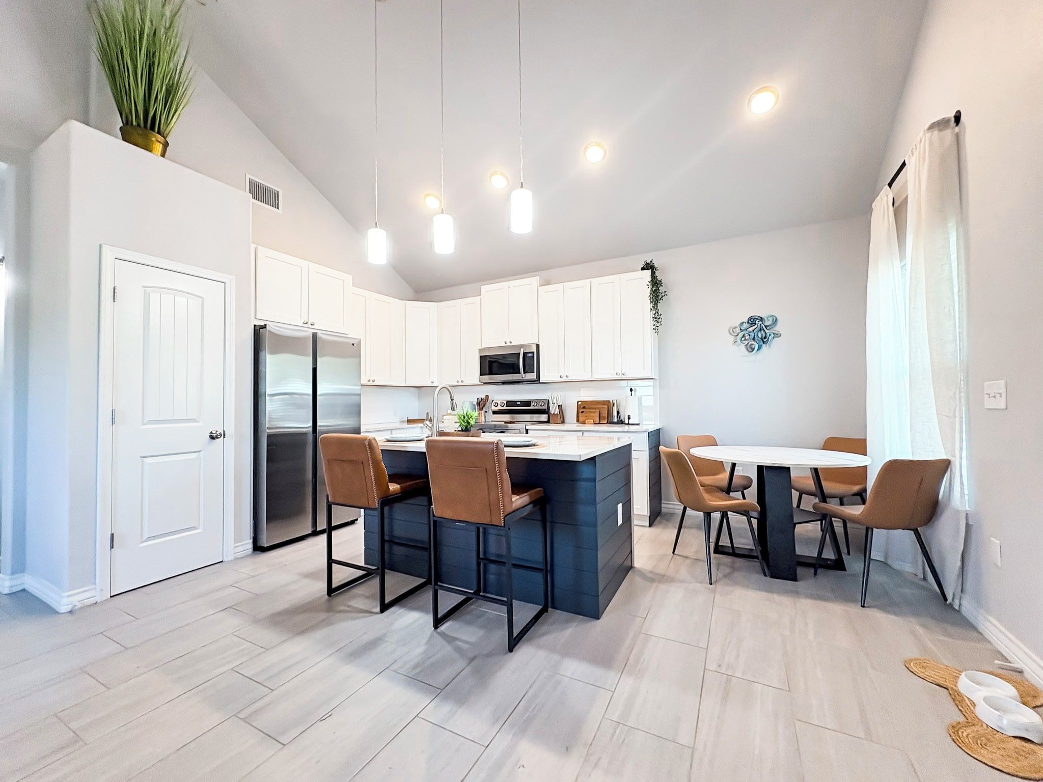 A modern kitchen with white cabinets, a central island, and a dining area with chairs.