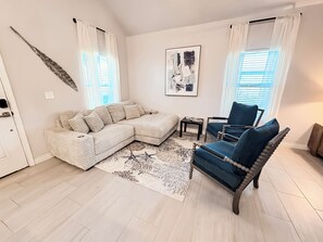 A living room with a sectional sofa, a blue armchair, a patterned rug, and a wall-mounted artwork. - Happy Heron Cottage-Dog-Friendly, Near Beach + Boat Parking, 2kayaks, BBQ Pit (Rockport)
