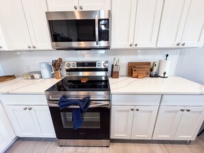 A kitchen with white cabinets, stainless steel appliances including a microwave and oven, and a countertop with various kitchen utensils and appliances. - Happy Heron Cottage-Dog-Friendly, Near Beach + Boat Parking, 2kayaks, BBQ Pit (Rockport)