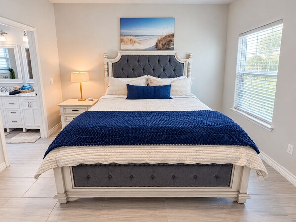 A bedroom with a large bed, a nightstand, a dresser, a window with blinds, and a painting on the wall. - Happy Heron Cottage-Dog-Friendly, Near Beach + Boat Parking, 2kayaks, BBQ Pit (Rockport)