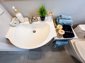 Een badkamer met een witte wastafel, een spiegel, een plant in pot en handdoeken.
