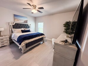 Een slaapkamer met een bed, nachtkastjes, een plafondventilator, een raam en een televisie.