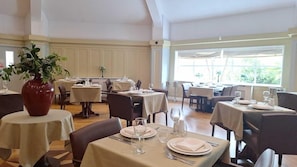 Ein Restaurant mit mehreren gedeckten Tischen, einer großen Vase mit Blumen und Blick auf Grünfläche.