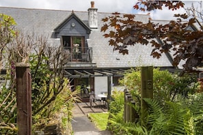 Ein Wohnhaus mit Backsteinfassade, einem Balkon und einem Gartenbereich mit Farne und Holzzaun.