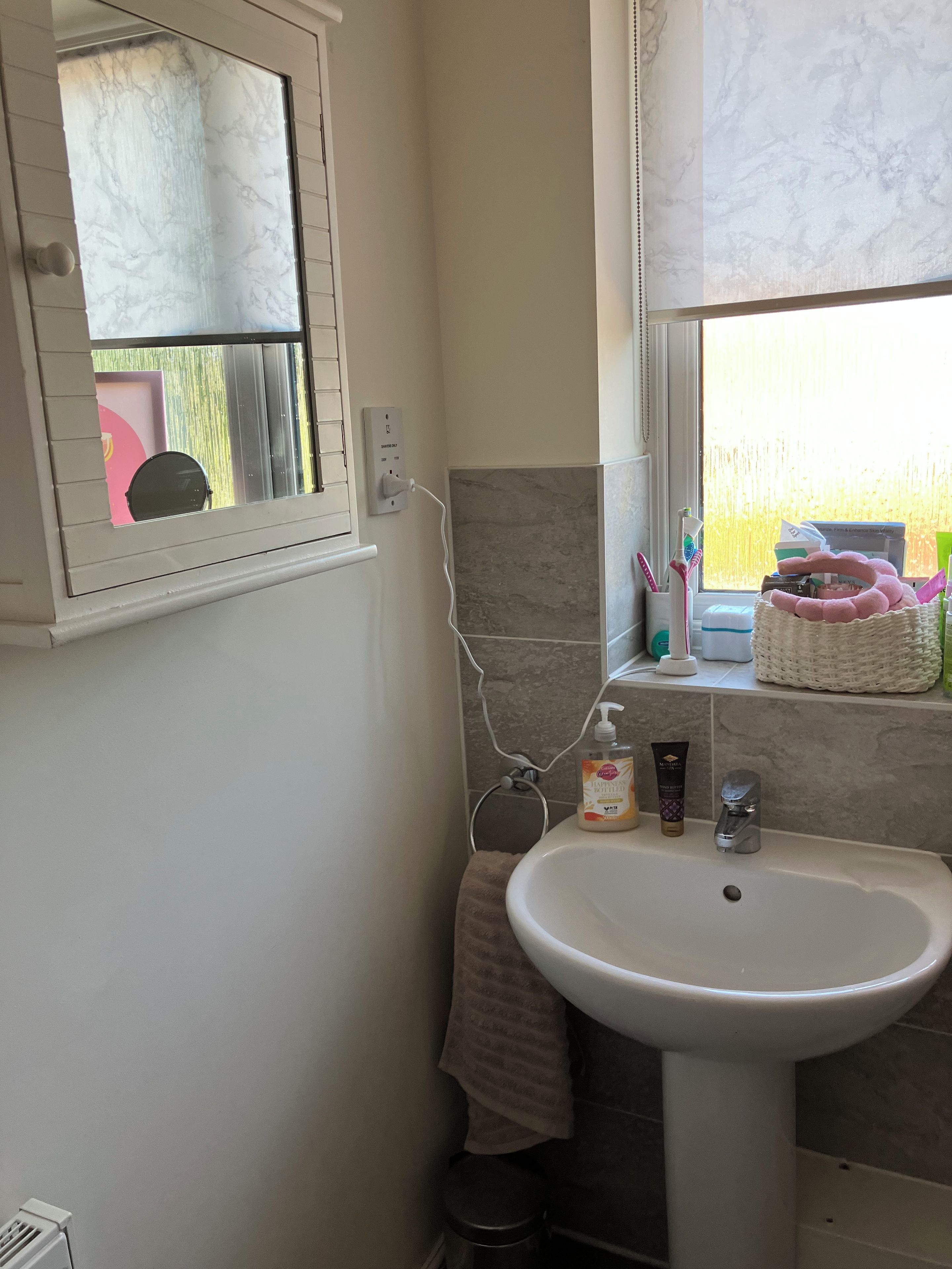 Et badeværelse med en hvid vask, et håndklæde hængende på væggen og toiletartikler på vindueskarmen.