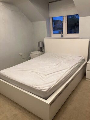 A bedroom with a single bed, a bedside table with a lamp, and a window with a view of buildings. - Two rooms and one bathroom available for short term rental. Free parking! (Hemel Hempstead)