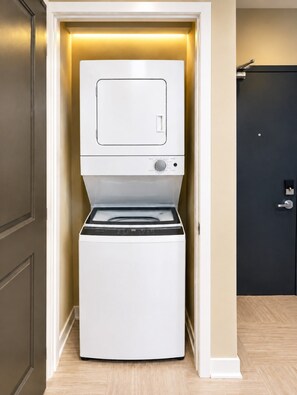A compact washer and dryer unit installed in a narrow hallway with a door on the right. - Magic City Oasis | 2 King 1 Queen 2B (Birmingham)