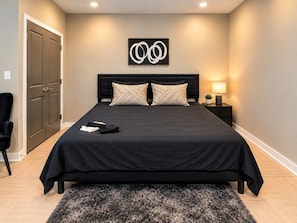 A bedroom with a large bed, a nightstand, a lamp, and a door. - Magic City Oasis | 2 King 1 Queen 2B (Birmingham)