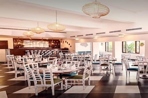 A restaurant with multiple dining tables and chairs, overhead wicker chandeliers, and a bar area in the background. - Otium Resort by the Oterra (Alto de Porvorim)