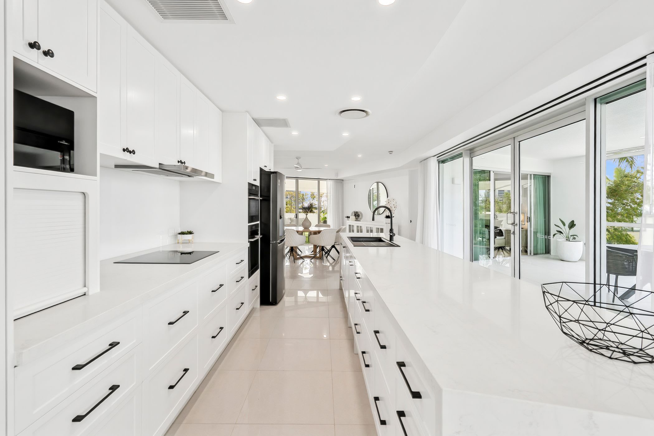 A modern kitchen with white cabinetry, a central island, and a dining area with a view.