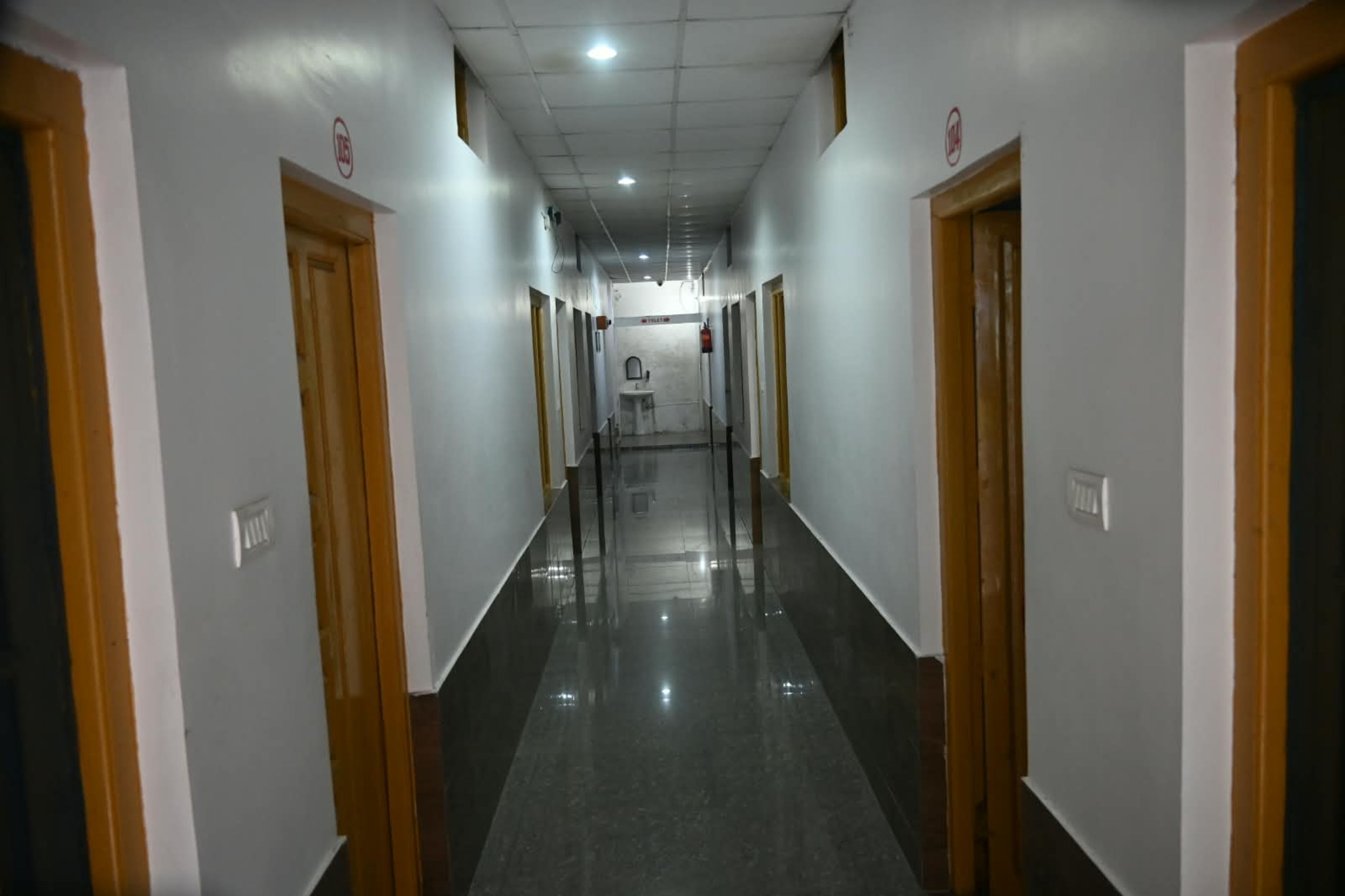 A long, narrow hallway with doors on both sides, leading to a central area with a sink and a mirror.