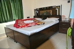Ein Bett mit einer weißen Matratze, einer roten und goldenen Decke und einem Kopfkissen. Dazu ein Holz-Kopfteil mit einer verzierten Platte und ein Gemälde darüber.