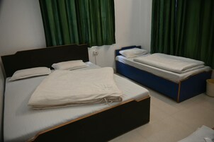 Una habitación con dos camas, una con cabecera oscura y otra con cabecera azul, ambas con ropa de cama blanca.