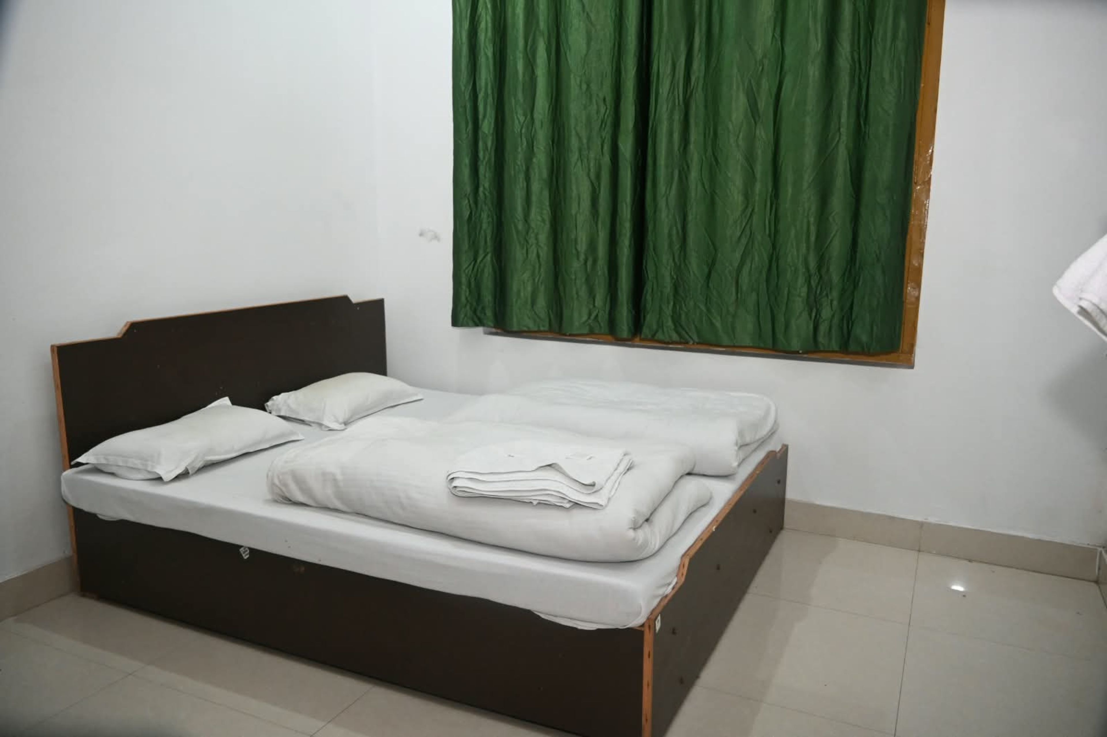 A single bed with white bedding in a room with white walls and a green curtain.