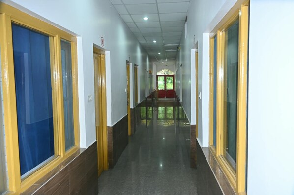 Un largo y estrecho pasillo con puertas a ambos lados, que conduce a una habitación con alfombra roja y un amplio ventanal al final.