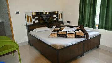 A single bed with a patterned headboard, a green chair, and a window with green curtains.