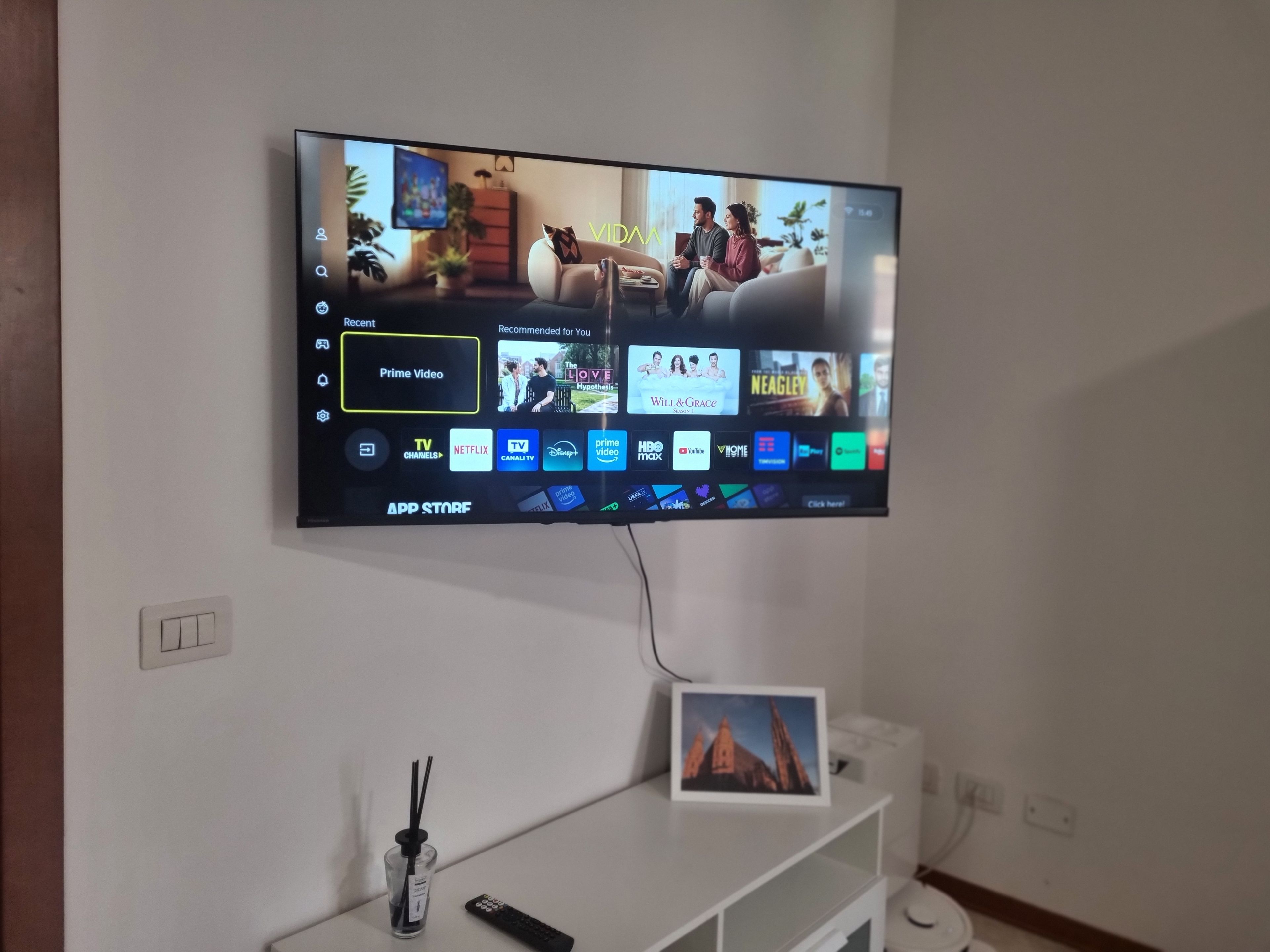 Una TV a schermo piatto montata a parete mostra l'interfaccia di un'app di streaming con diverse opzioni di contenuto.