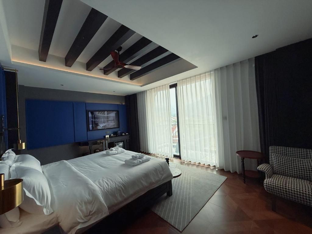 A modern hotel room with a large bed, a flat-screen TV, a ceiling fan, and a view of the outdoors through large windows.