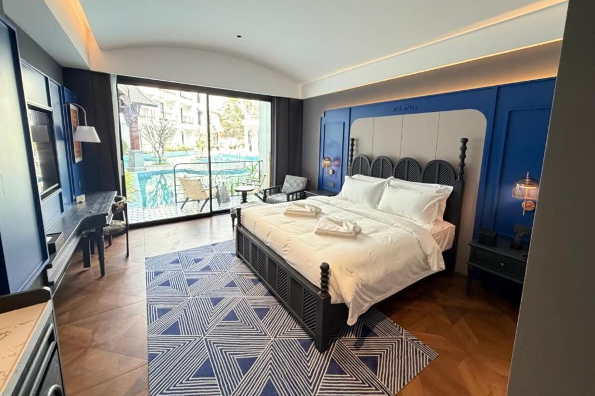 Una camera d'albergo moderna con un letto grande, un'area pranzo e vista sulla piscina.
