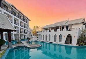 Hotel com piscina, várias varandas e céu ao pôr do sol.