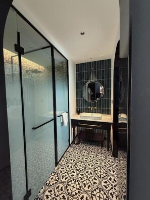 Un bagno con box doccia in vetro, un lavandino con specchio sopra e piastrelle decorative sul pavimento.