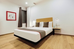 A hotel room with a large bed, a bedside table with a phone, a framed picture on the wall, and a window with curtains. - Townhouse Golden Avenue Road (Amritsar)