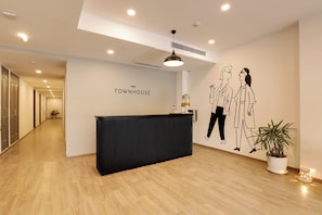 A reception area with a black reception desk, a wall-mounted sign reading 'OYO TOWNHOUSE', and a minimalist decor including a potted plant and a wall art of two figures. - Townhouse Golden Avenue Road (Amritsar)