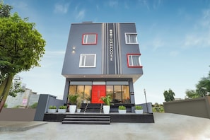 Een modern, tweelaags gebouw met een rode deur, grote ramen en een trap die naar de ingang leidt.