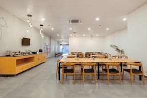 A spacious dining area with wooden tables and chairs, a kitchen counter with appliances, and a large window providing natural light. - Townhouse Golden Avenue Road (Amritsar)