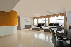 A spacious hotel room with a large bed, a sofa, a dining table with chairs, and a view of the city through large windows. - Hotel O Teg Royal (Amritsar)