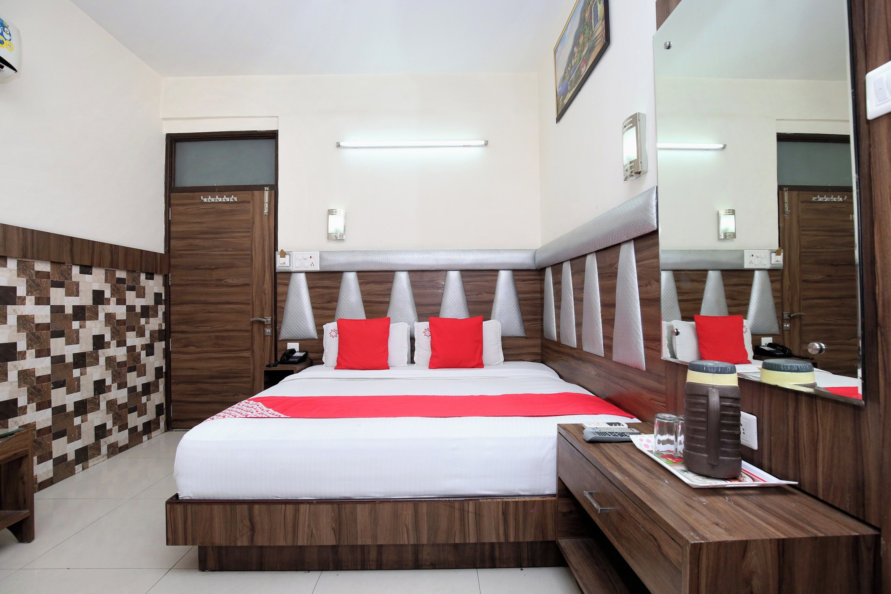 A hotel room with a large bed, a wooden headboard, a bedside table, a mirror, and a tiled wall.