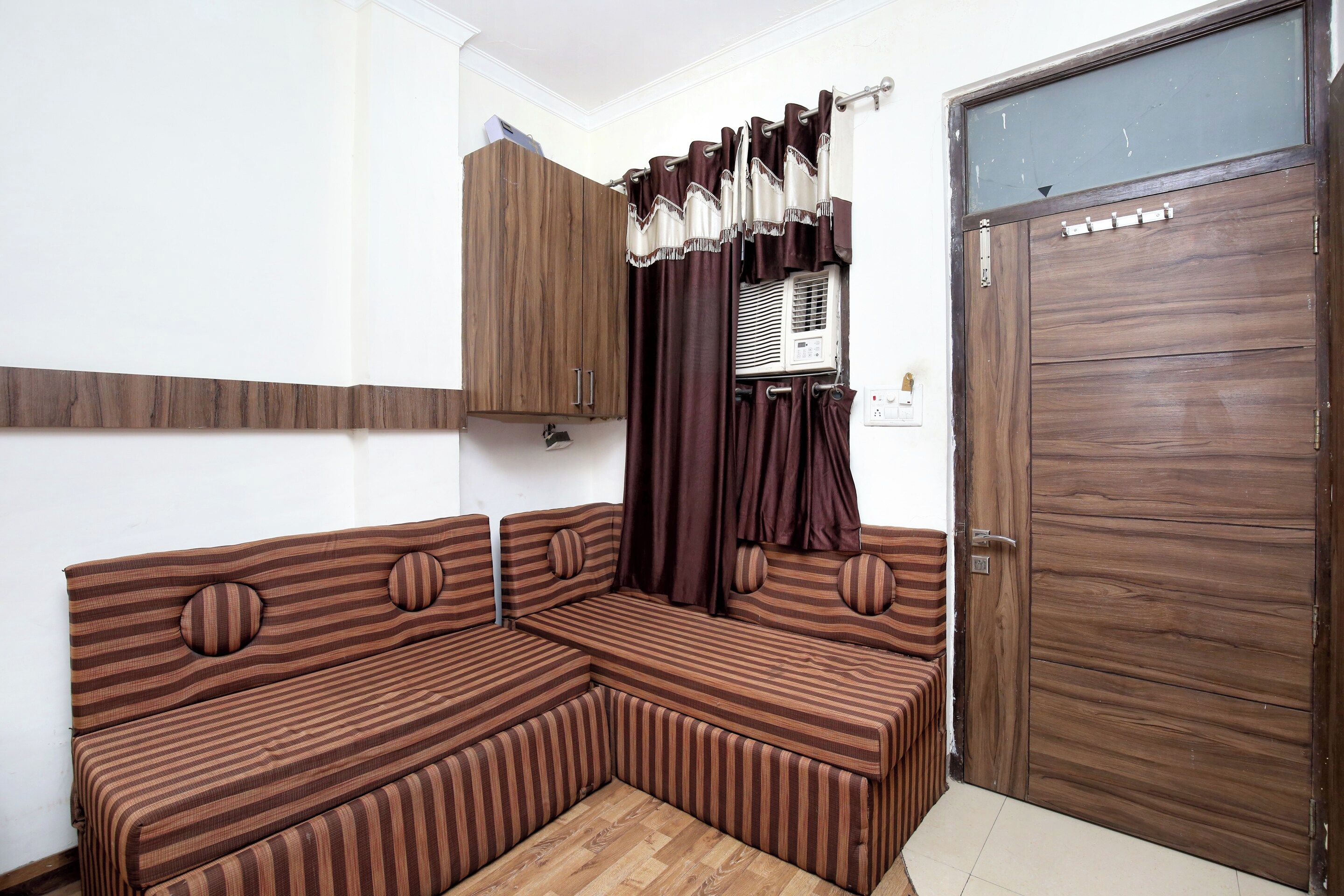 Una habitación con un sofá modular, un armario de madera, una puerta y un ventanal con cortinas.