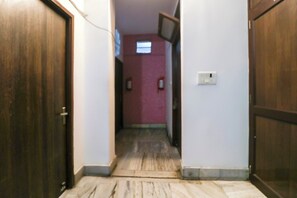 Un pasillo estrecho con puertas de madera a ambos lados, suelo de baldosas y una pared rosa con una ventana.