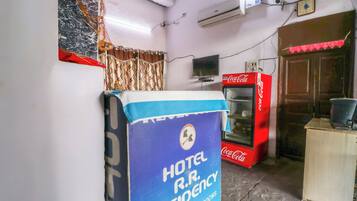 Ett rum med en stor, blå skylt med texten Hotel R.R. Residency, ett kylskåp från Coca-Cola och en tv som är monterad på väggen.
