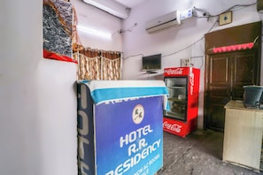 Ein Zimmer mit einem großen, blauen Schild für Hotel R.R. Residency, einem Kühlschrank von Coca-Cola und einem an der Wand befestigten Fernseher.