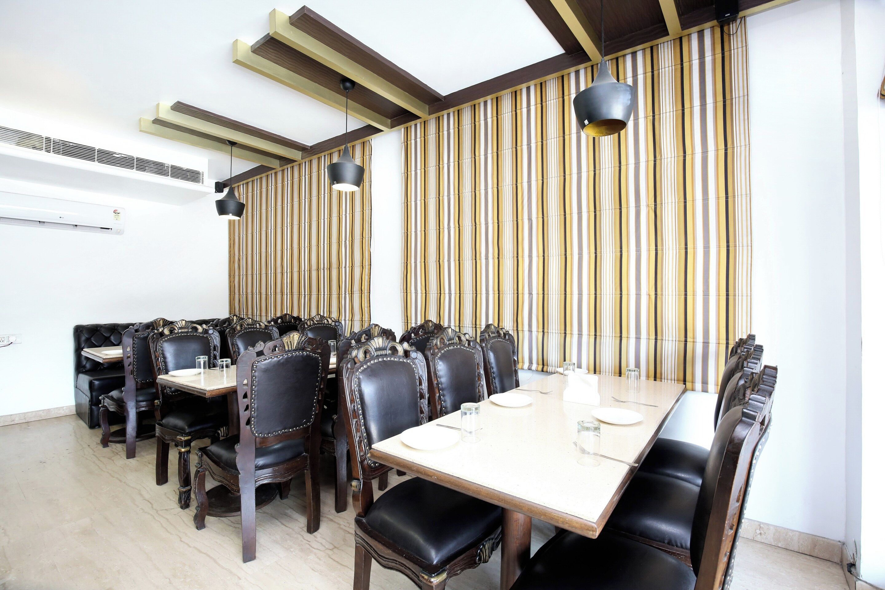 Uma sala de jantar com uma mesa comprida e várias cadeiras, teto com vigas aparentes e um pano de cortina listrado ao fundo.