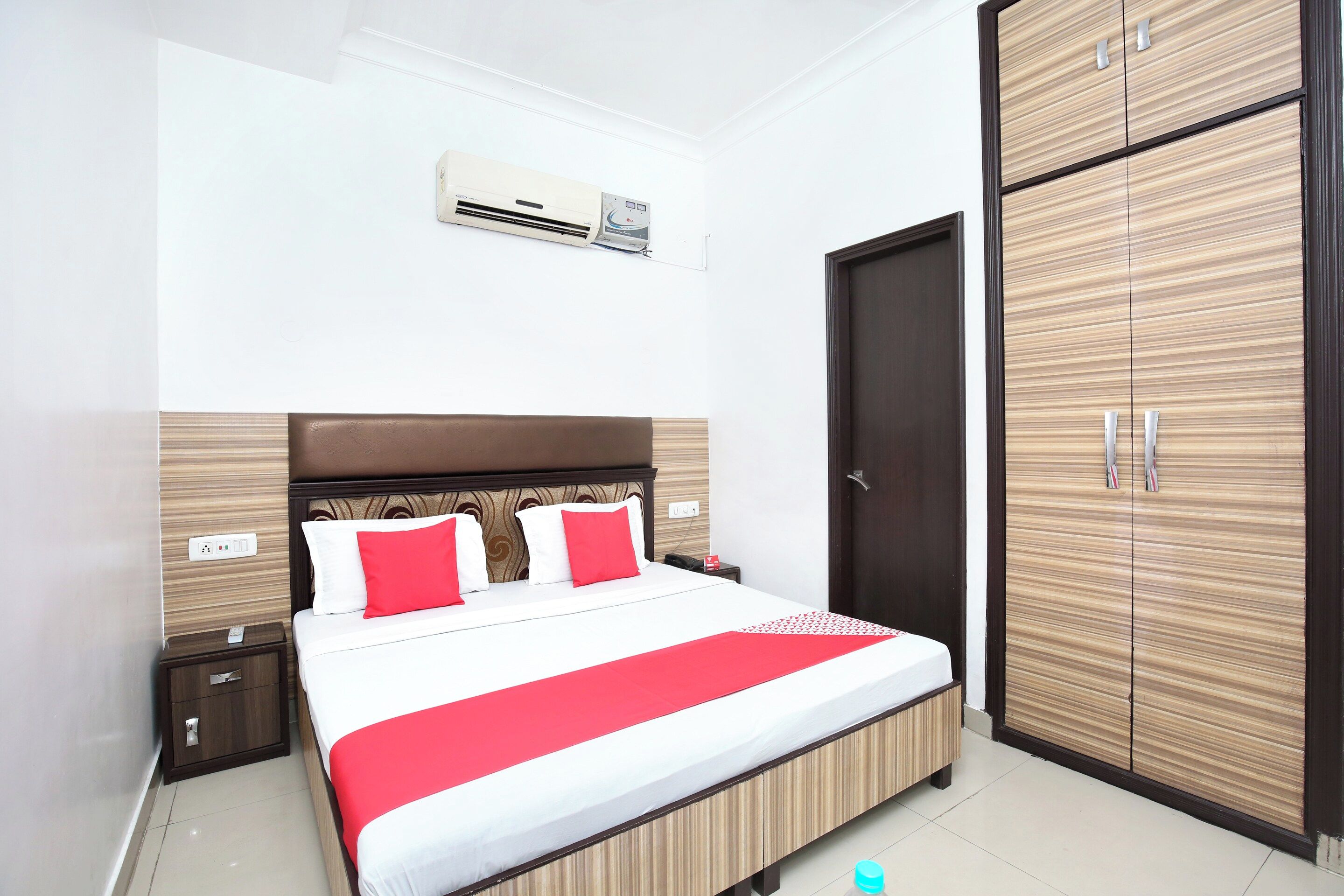 Quarto de hotel com cama, mesas de cabeceira, ar condicionado, guarda-roupa e porta.