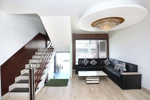 Un salon moderne avec un escalier, un canapé en cuir noir, une table basse en verre et un lustre.