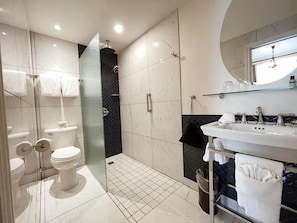 Une salle de bain moderne avec une douche à parois de verre, des toilettes blanches, un lavabo avec une étagère en verre et un miroir au-dessus du lavabo.