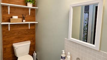 Een badkamer met toilet, wastafel, spiegel en planken met toiletartikelen.
