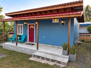 Ein Haus mit roter Tür, blauen Wänden und einer Veranda mit zwei Stühlen und einer Fußmatte.