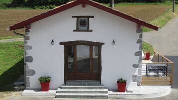 A small, single-story building with a red roof, a wooden door, and two potted plants on the ground floor.