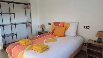 Un letto rifatto con cura, coperta a motivi geometrici, due comodini con lampade e una mensola a muro con appendiabiti.