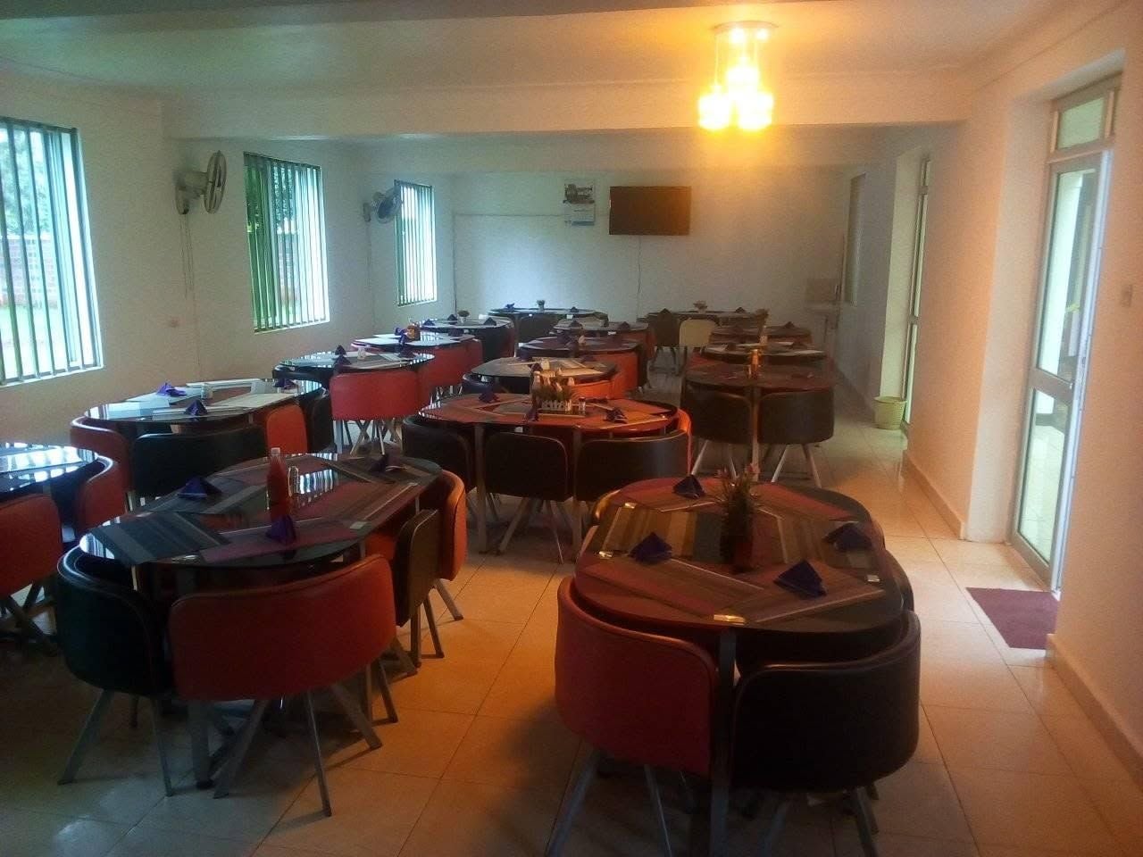 Une salle de classe avec des tables et des chaises rondes, un écran de projection et des fenêtres équipées de stores.