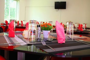 A dining table set with clear glassware, a white vase with orange flowers, and red napkins. - Bilkon Hotel Jinja (Jinja)
