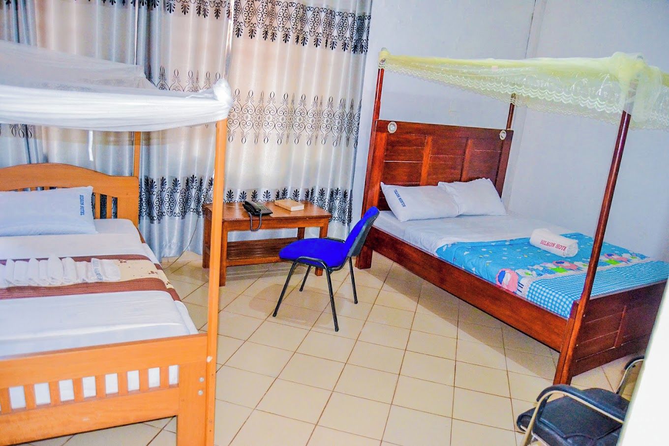 A room with two single beds, a desk with a chair, and a window with curtains.