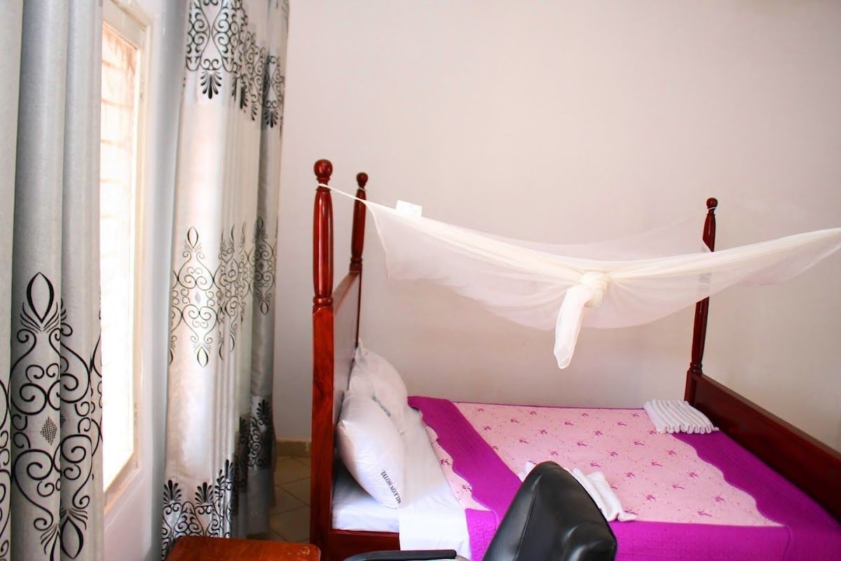 Una cama individual con dosel, una almohada, un edredón y una silla en una habitación con cortinas estampadas.