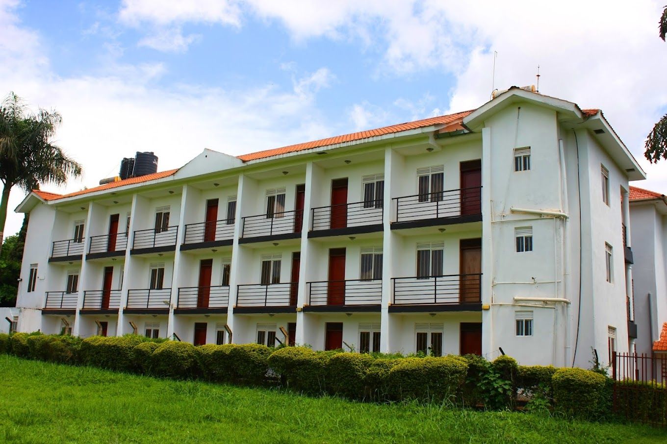A multi-story building with balconies, a red-tiled roof, and a green lawn in the foreground.