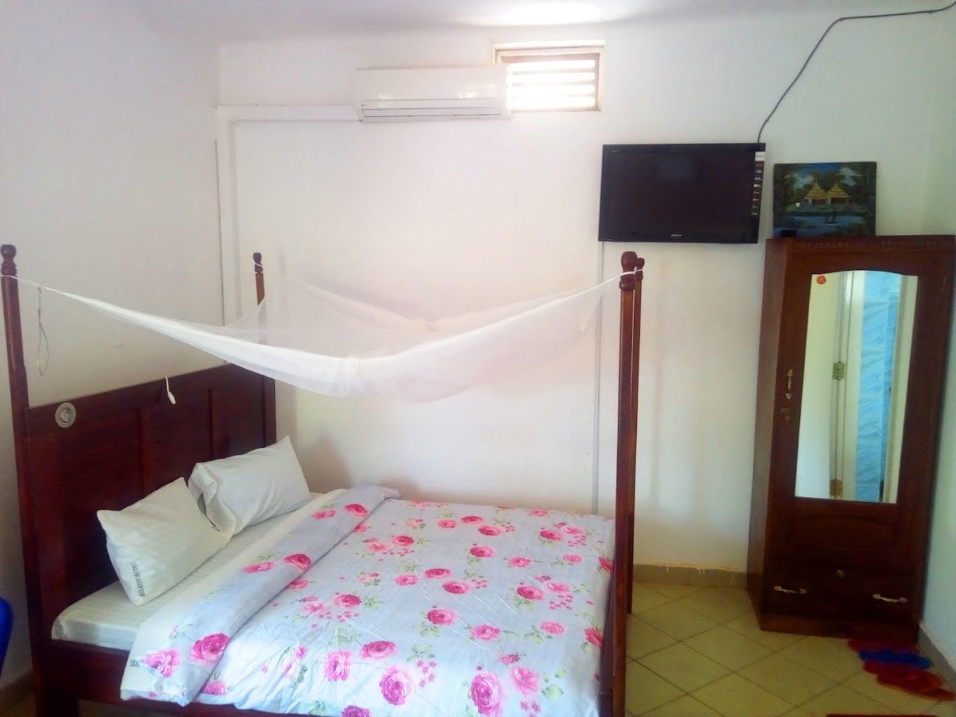 Une chambre à coucher avec un lit, une armoire en bois, un téléviseur et une fenêtre avec des stores.
